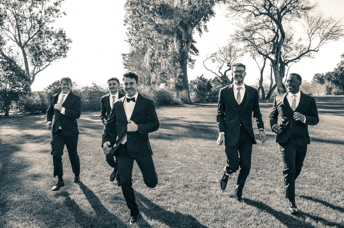 Groomsmen in black suits running across a field